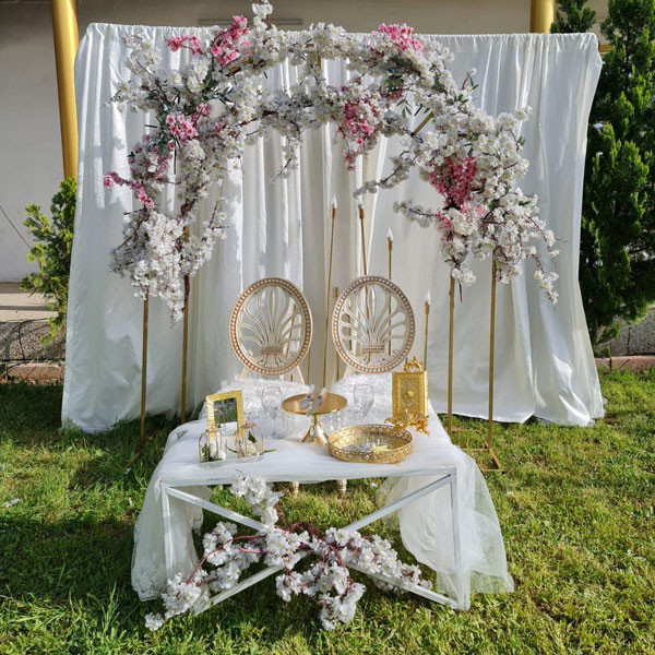 White Shade Wedding Decoration with Big Table, 2 Elegant Chairs, Gate Round Metallic Stand Decorated with Flowers & White Sheet Background, Candle Sticks, etc..