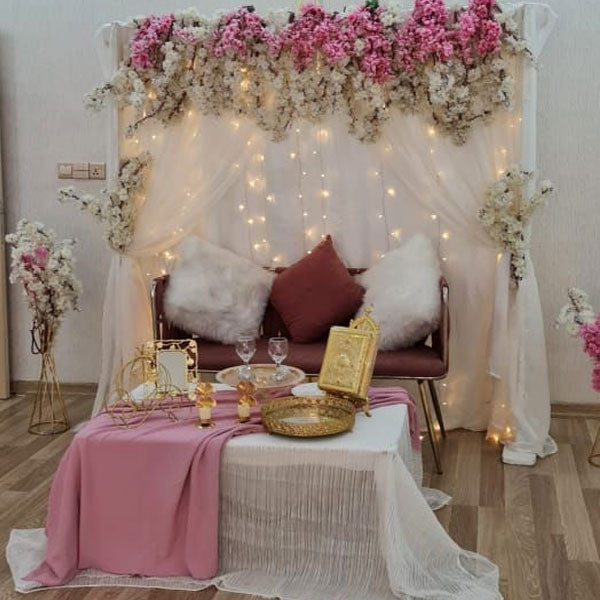 White Shade Wedding Decoration with Big Table & 2 Metallic Vases, Couch with Fiery Pillows & Seat, Gate Square Metallic Stand Decorated with Flowers & Sheet, etc…